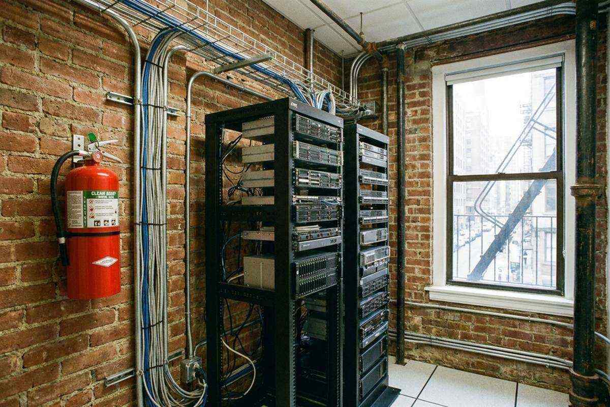 Wall-mounted clean agent fire extinguisher beside server racks in a NYC office server closet