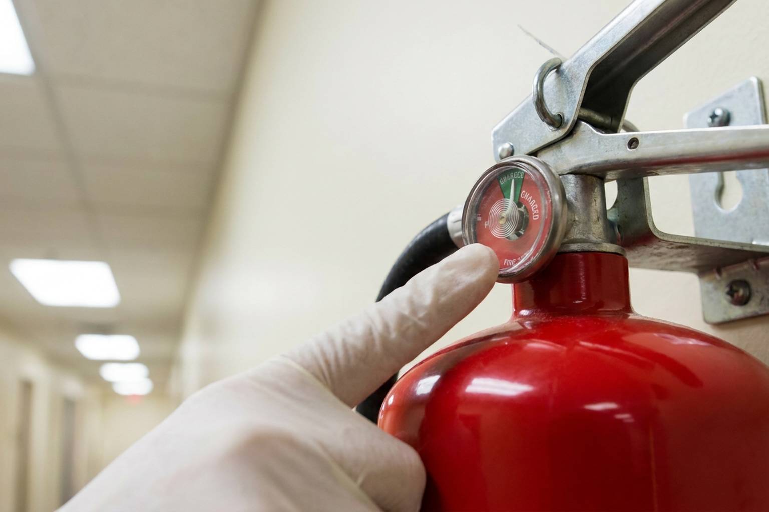 Technician checking the pressure gauge on a wall-mounted fire extinguisher during monthly inspection